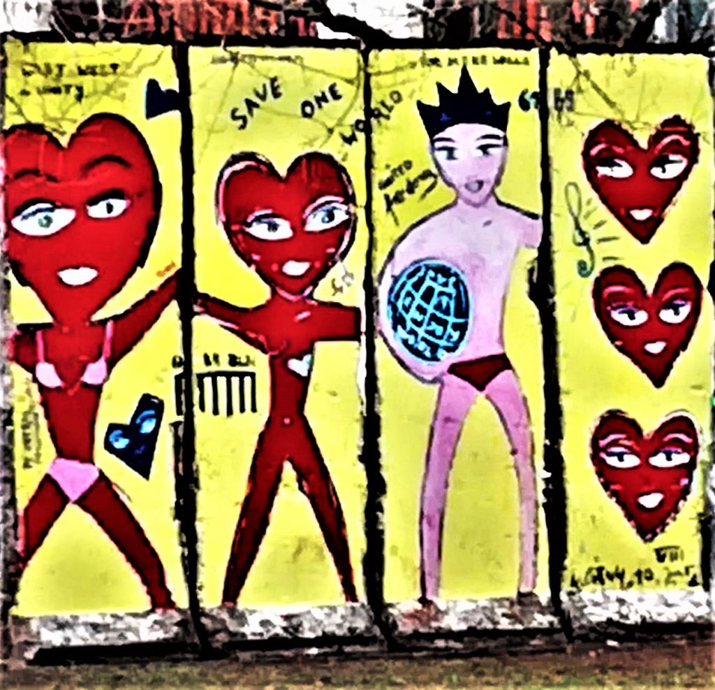 Graffiti sur un pan du mur de Berlin représentant un jeune homme tenant un ballon, deux personnages avec une tête de coeur et 3 coeurs